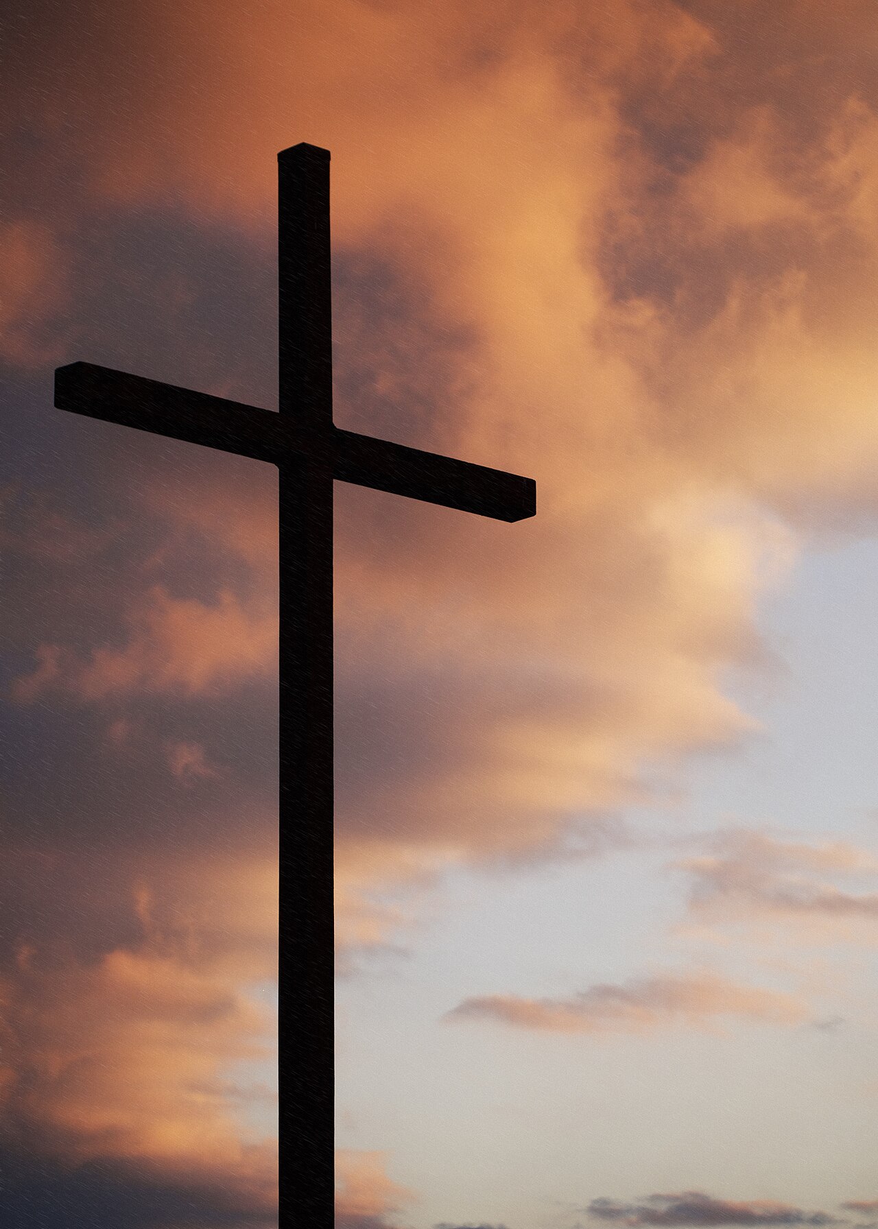 A simple wooden cross silhouetted against a sunset sky